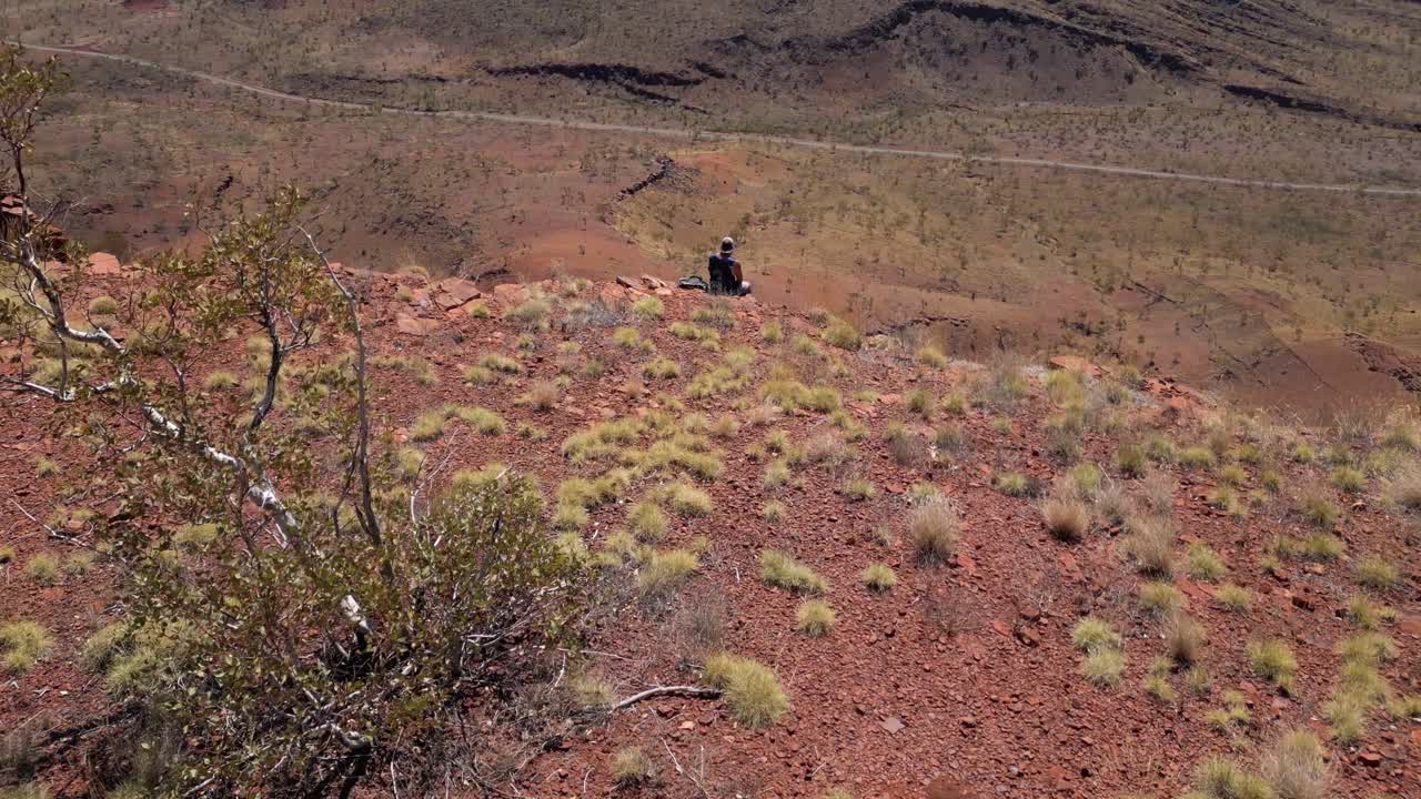 disparo aéreo de un excursionista masculino sentado en el borde de un pico en las montañas del desierto australiano en verano