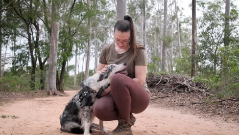 Frau-Mit-Brille-Vergnügt-Sich-Mit-Ihrem-Haustier-Im-Wald,-Einem-Australischen-Schäferhund,-Streichelt-Ihn-Und-Küsst-Ihn