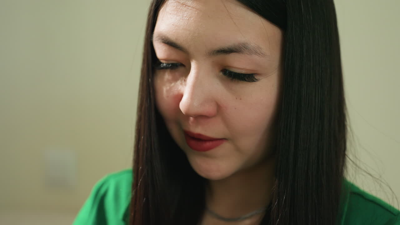 mujer asiática reflexiva, retrato en interior de mujer pensativa, material mira a mujer en vestido verde elegante en interior, entorno interior que muestra a mujer reflexiva vestida de verde con pelo oscuro