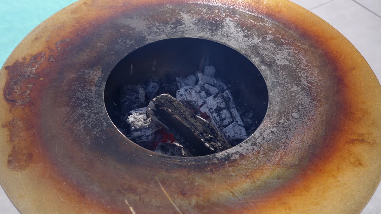 Brasas calientes brillan bajo la parrilla metálica mientras el calor asciende