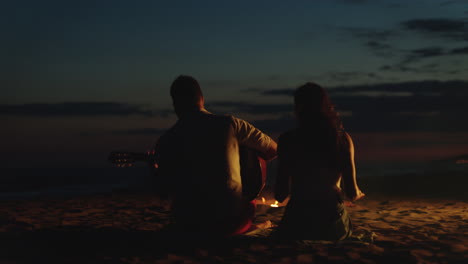 pareja romántica tocando la guitarra en la playa por la noche