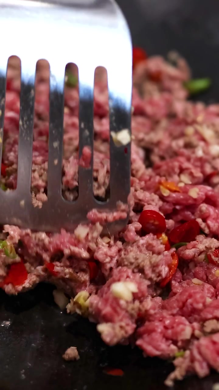 Nahaufnahme von Rindfleisch, das mit Gemüse in einer Pfanne angebraten wird. Helle Beleuchtung betont lebendige Farben und Texturen.