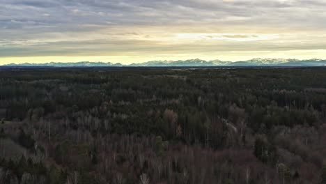 Im-Gebirge---Drohnenflug-Rückwärts-über-Einen-Weiten-Wald-Mit-Sonne-Hinter-Wolken