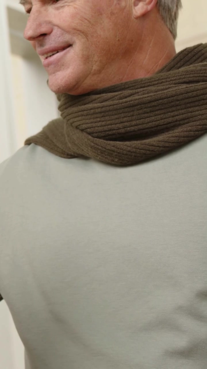 Video verticale: Uomo che si gira e risponde a una mano sinistra che offre un oggetto vicino alla facciata, con sciarpa e spazio per il testo.
