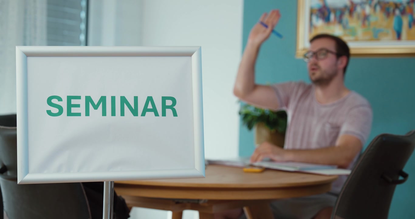 Man raising his hand during a seminar, representing education, training, participation, learning, questions, and professional development.