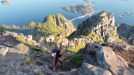 a young, fit woman is climbing up the cliff of festvågtind mountain with her backpack and hiking boots