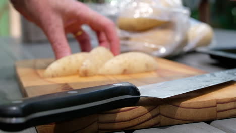 female hands slicing potato into thick cut fries on a wooden chopping board