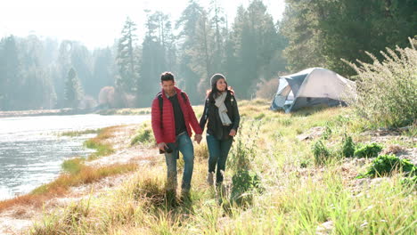 couple holding hands walking near lake on a camping trip