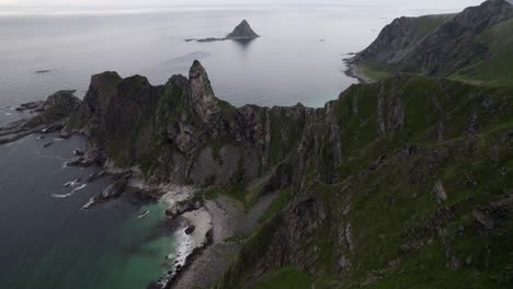 Droneshot-tilting-upwards-flying-over-mountainrange-seperating-two-beaches-with-bird-island-in-background