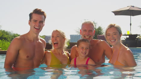 Retrato-De-Una-Familia-Multigeneracional-Sonriente-En-Vacaciones-De-Verano-Relajándose-En-La-Piscina