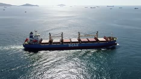 a cargo ship moves steadily through peaceful waters while other vessels are anchored in the distance, showcasing the busy shipping lane in daylight.