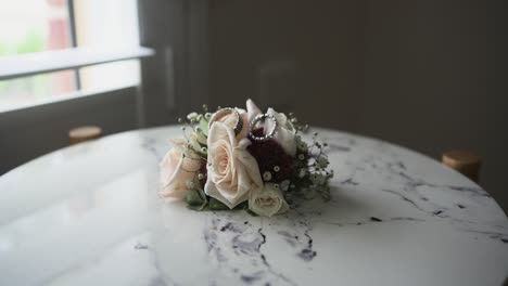 Pequeño-Ramo-De-Flores-De-Boda-Colocado-Sobre-Una-Mesa-Cerca-De-La-Ventana-A-La-Luz-Del-Día-Con-Dos-Anillos-De-Boda-Encima