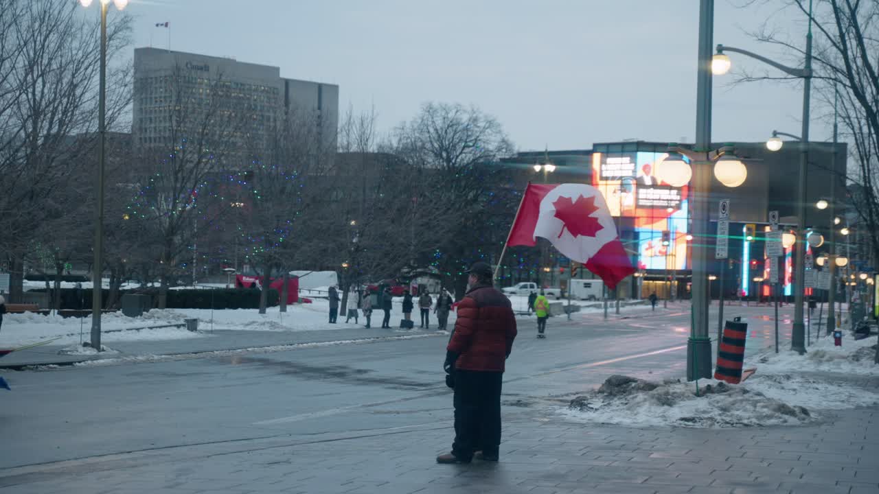 Man Waving Canadian Flag In The Sidewalk At Winter During Freedom Convoy In Canada. - wide shot