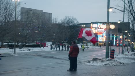 man waving canadian flag in the sidewalk at winter during freedom convoy in canada. - wide shot