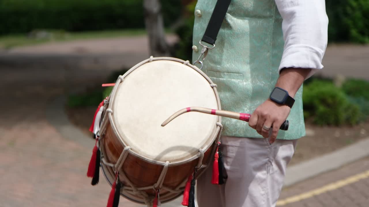 Close-up of a musician playing a dhol drum at an Indian wedding. Rhythmic beats, colourful tassels, and vibrant attire capture the joyful spirit of traditional celebration