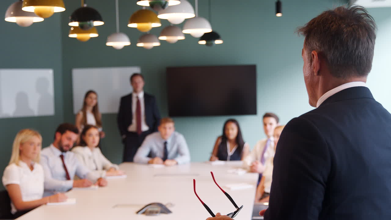 성숙 한 사업가 가 졸업생 채용 평가 날 에 테이블 주위 집회 를 연설 하고 있다