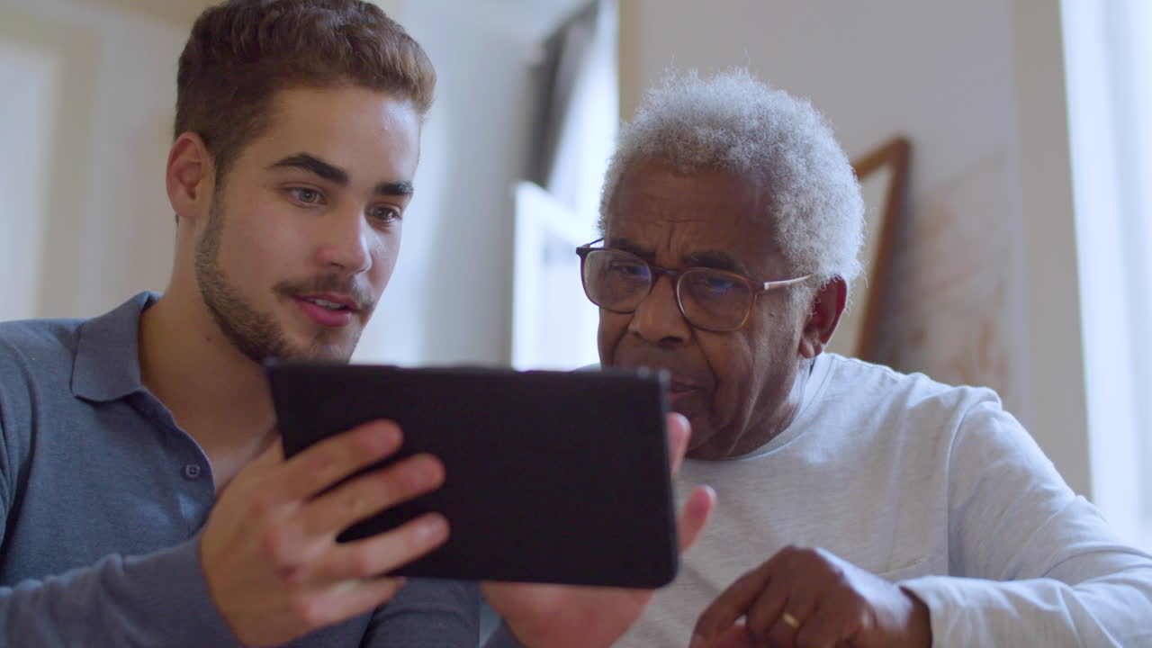 Young Caucasian guy helping his grandpa with using tablet.