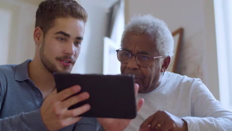 young caucasian guy helping his grandpa with using tablet.