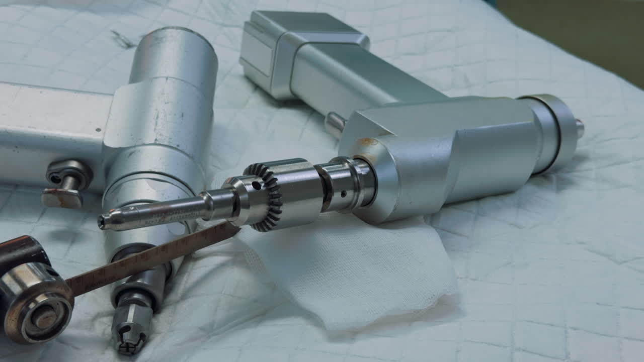 Surgeon's gloved hands preparing metal prosthetic components on a sterile blue cloth. A close-up view of the instruments and implants used for an orthopedic procedure
