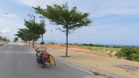 hombre montando en moto con tabla de surf en indonesia, sigue la vista trasera