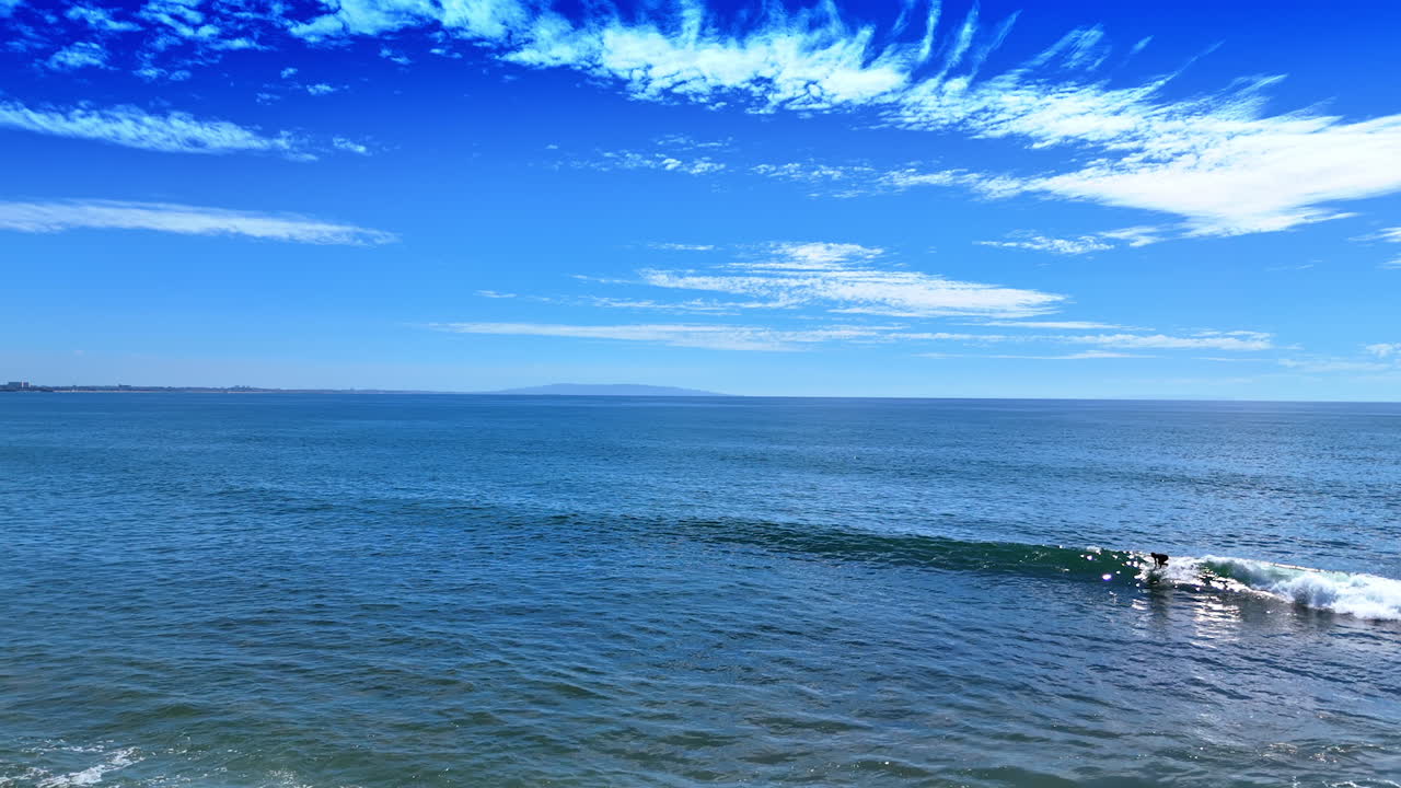 Surfers ride the waves on sunny day. View on the beautiful blue waterscape and sky with cirrus clouds