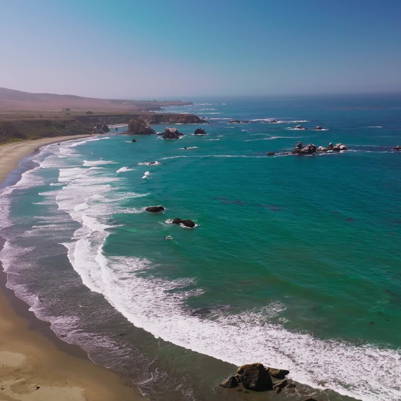 Beautiful hypnotizing foamy waves arriving to the sandy beach. Rocky shore covered with grass. Some stones peeping from water. Aerial view