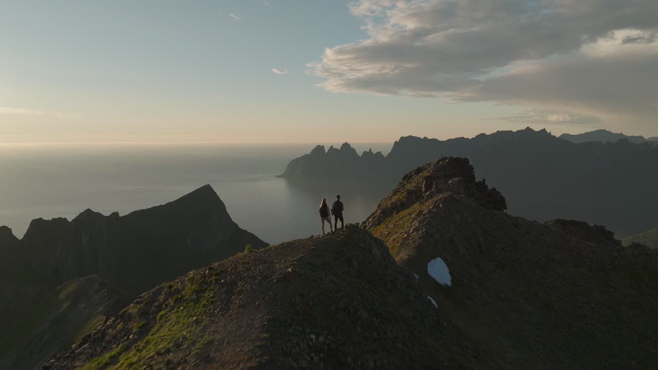 A young couple hiking on Husfjellet in Senja, Norway, at sunset with stunning mountain views