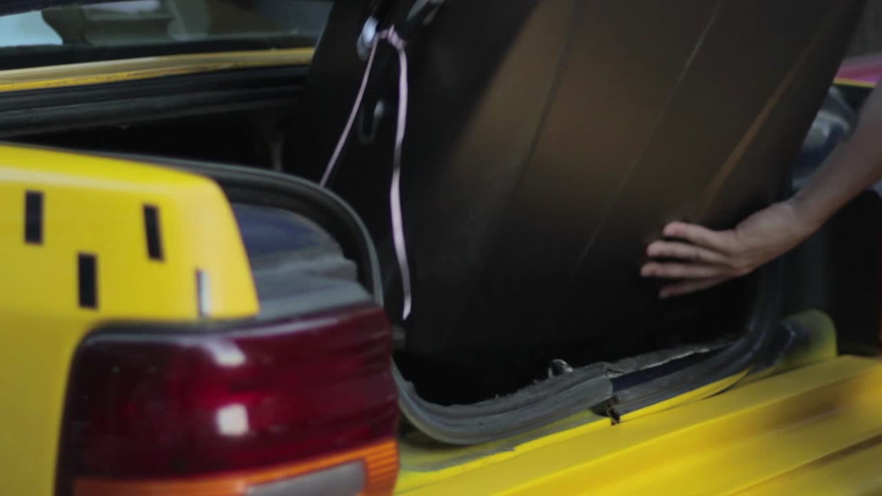 Person laster koffert inn i bagasjerommet på en gul taxi