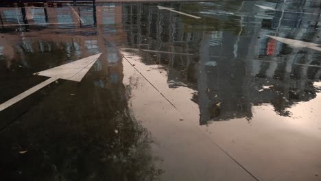una toma de edificios reflejados en hormigón húmedo cerca de un signo de flecha