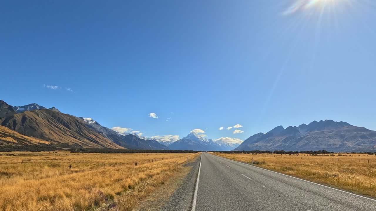 A long road leading towards snow-capped mountains under a clear blue sky