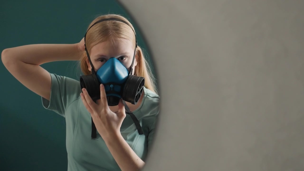 Caucasian woman in mirror prepping respirator before deep clean, quiet bedroom setting, teal wall and round mirror, careful strap and filter inspection, calm focused homeowner preparing safety gear