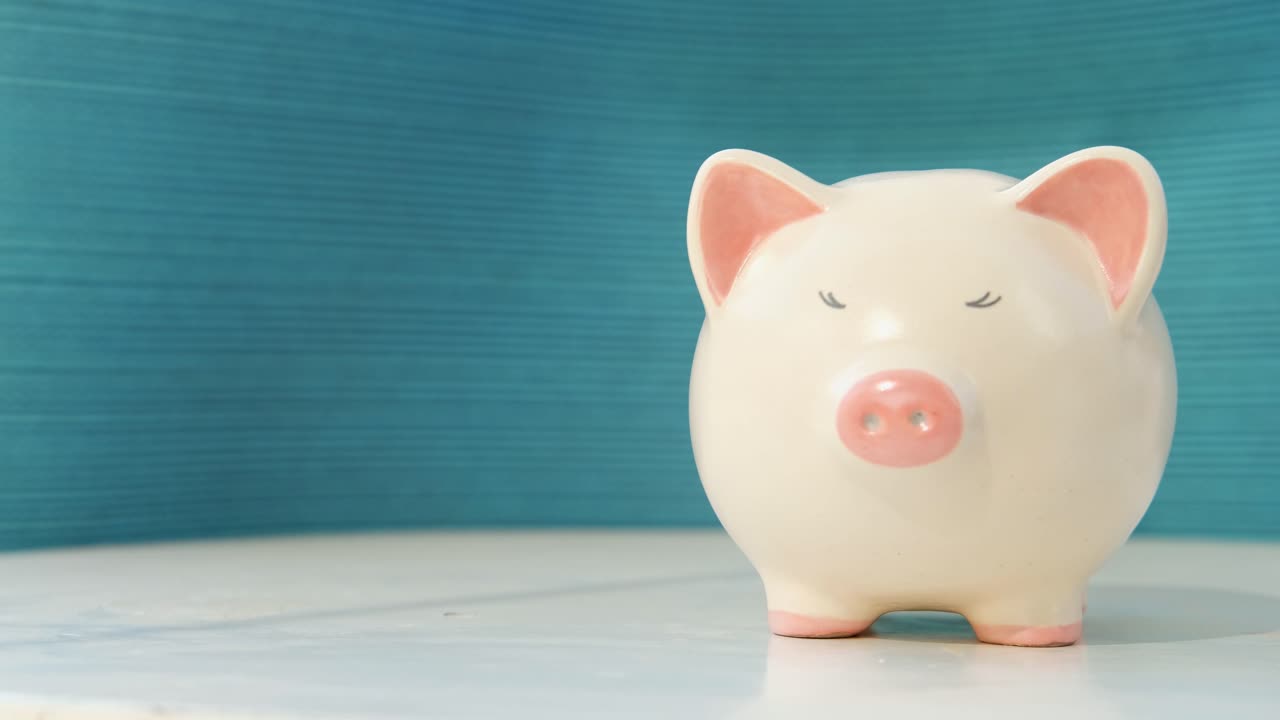 Saving money in a pig, Inserting coin inside pig coin box, hand putting coins in piggy bank isolated on blue background, closeup. money savings