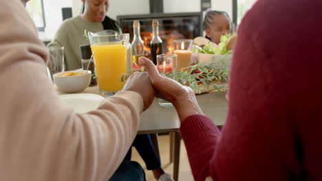 happy african american multi generation family praying at thanksgiving dinner, slow motion