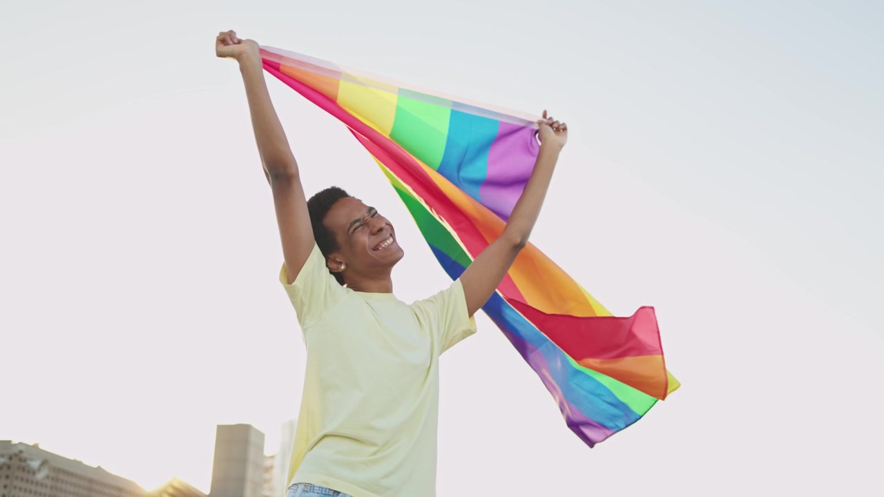 Happy Young Man Waving Rainbow LGBTQ+ Pride Flag Outdoors