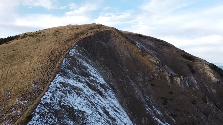 Droneudsigt over en grøn bakke med lidt sne, med en blå himmel og et par skyer i de schweiziske bjerge.