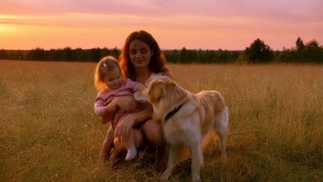 a mother, child, and dog in a field at sunset