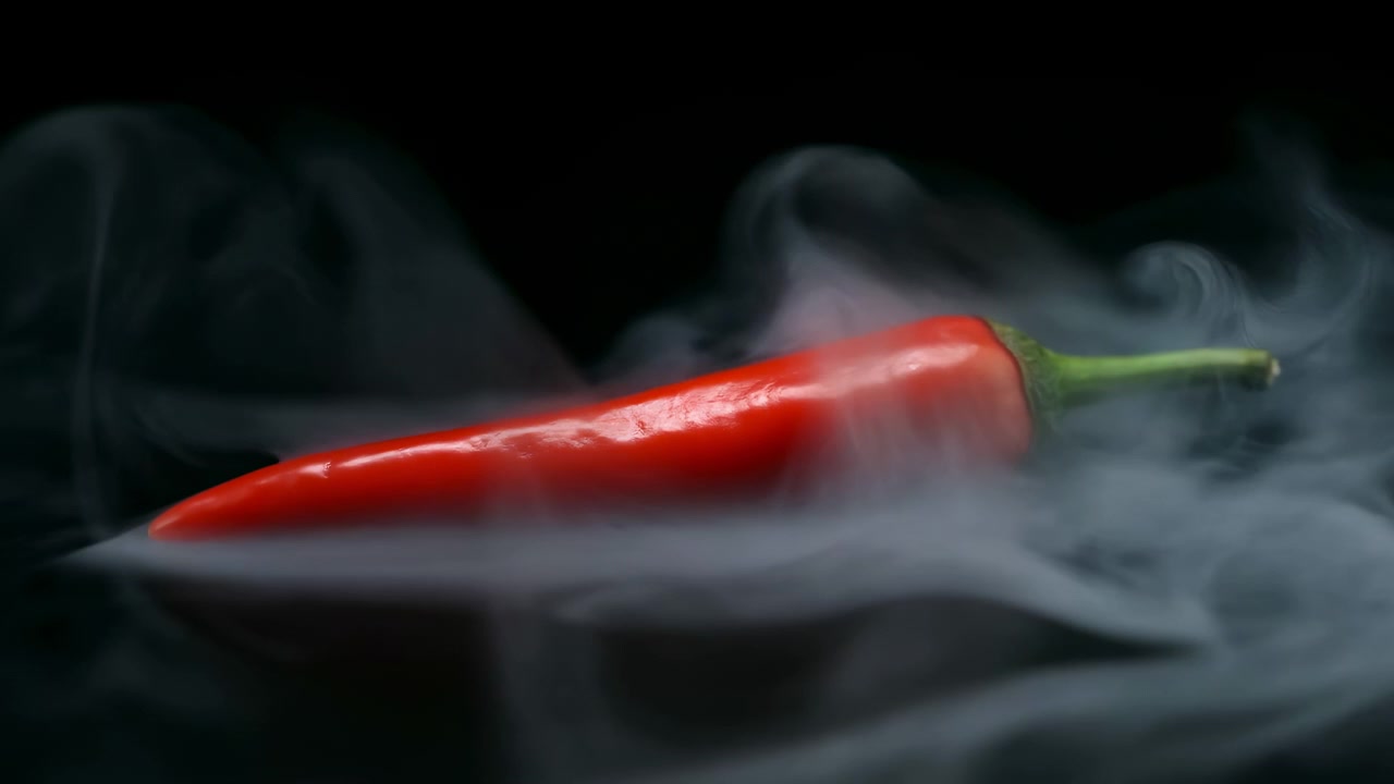 Uma única pimenta vermelha repousa sobre um fundo escuro, cercada por fumaça translúcida e ondulante, reflexos brilhantes, um talo verde nítido e um rico contraste de baixa luminosidade para uma cena de natureza morta de comida com atmosfera