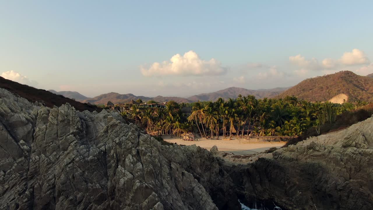 exuberantes palmeras y olas salpicando enormes rocas en playa maruata en una tarde soleada en michoacán, méxico