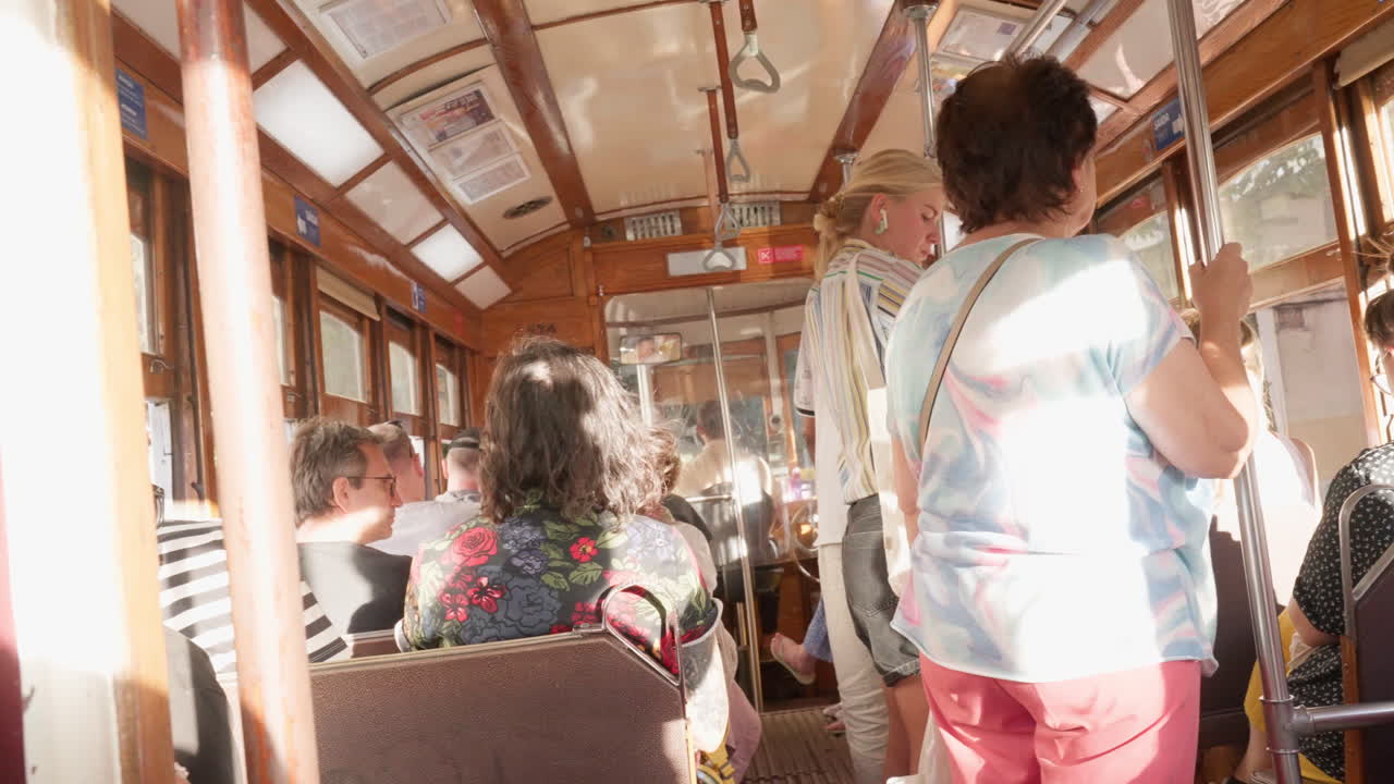 People transit in an electric trolley through the streets of Lisbon, Portugal, as passengers sit and hold on, with sun beaming through the windows, riding through the city's historic landscape.