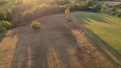 Observe-Cómo-Se-Pone-El-Sol-Sobre-Las-Ondulantes-Colinas-Del-Campo,-Arrojando-Un-Cálido-Y-Dorado-Brillo-Sobre-Los-Tranquilos-Campos-Y-Granjas-De-Abajo