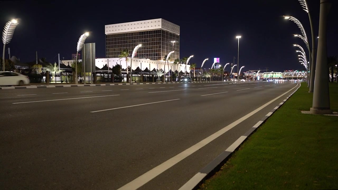 Accattivante B-roll automobilistico notturno. Veicoli viaggiano lungo una trafficata strada cittadina illuminata da lampioni luminosi unici e un imponente e moderno edificio governativo