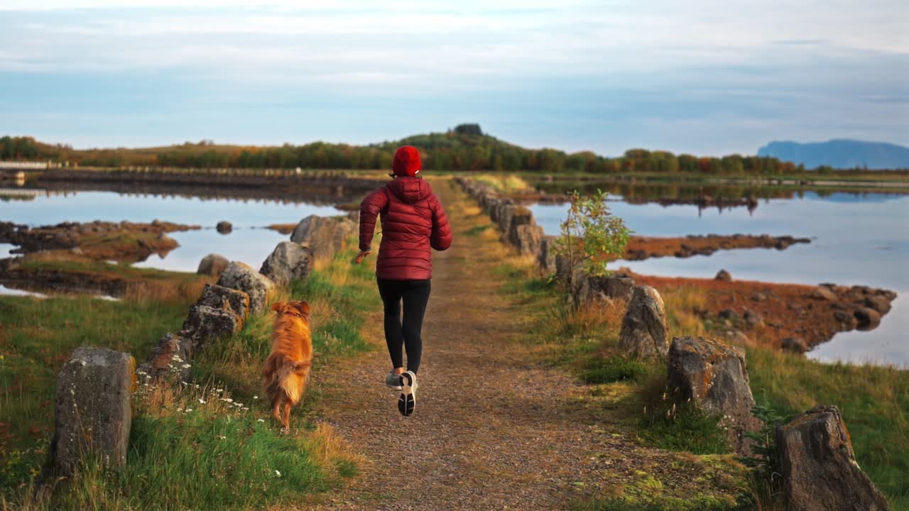 Running woman with dog along a scenic path near water, peaceful outdoor activity