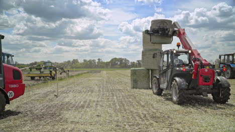 farming tractor loading haystacks on agricultural field