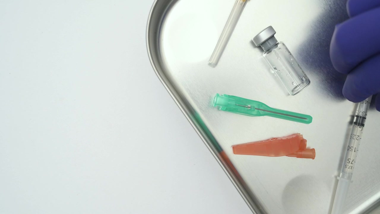 Healthcare worker picking up a syringe from a medical tray on a white background, top down view