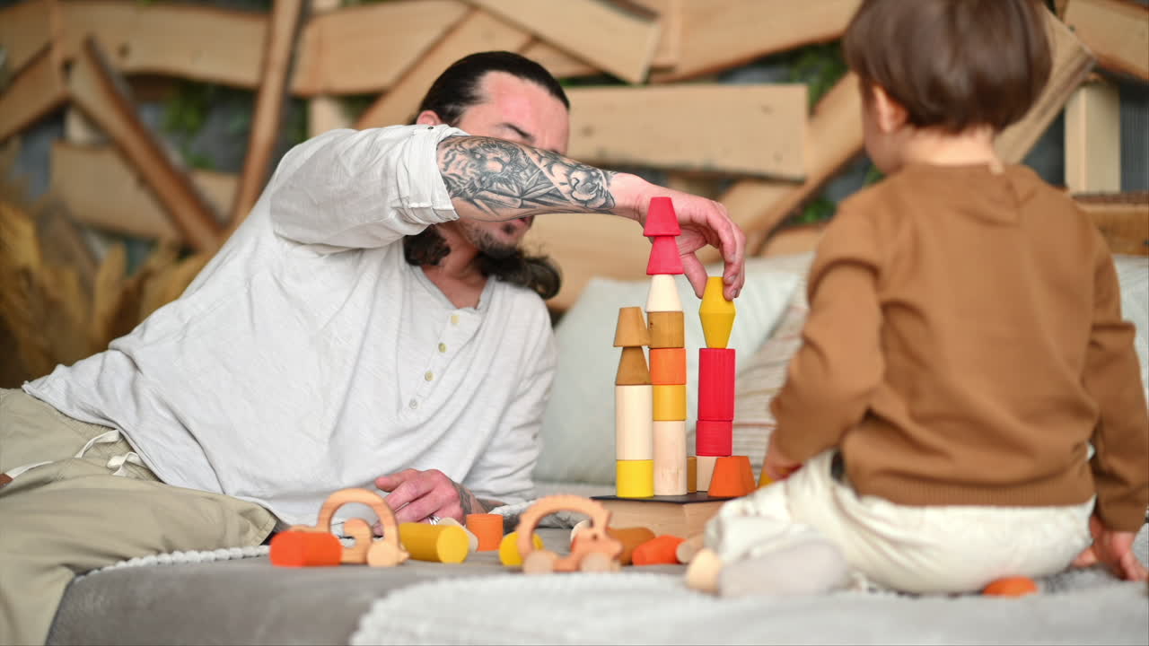 Father playing with his son with colourful, ecological wooden toys on the bed