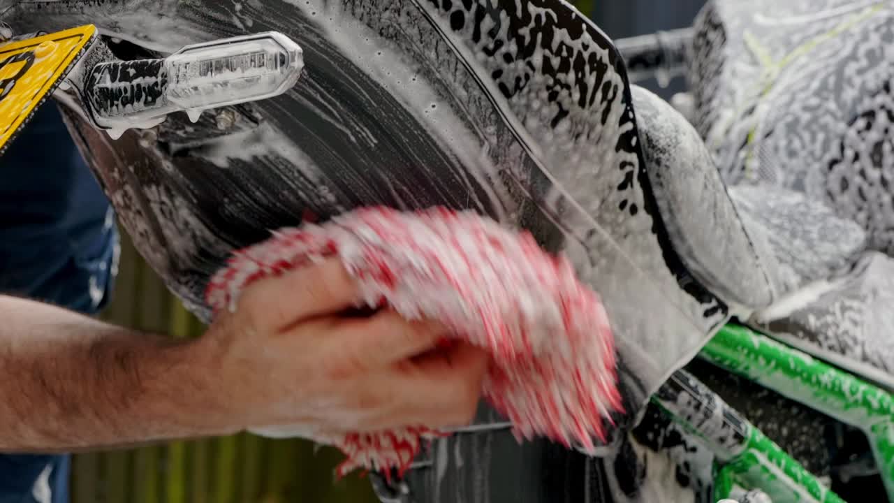 Cleaning rear of motorbike mud fender with snow foam shampoo