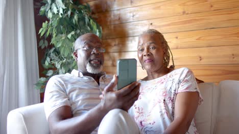 Glückliches-älteres-Afroamerikanisches-Paar-Mit-Smartphone,-Das-Zu-Hause-Auf-Dem-Sofa-Sitzt,-Zeitlupe