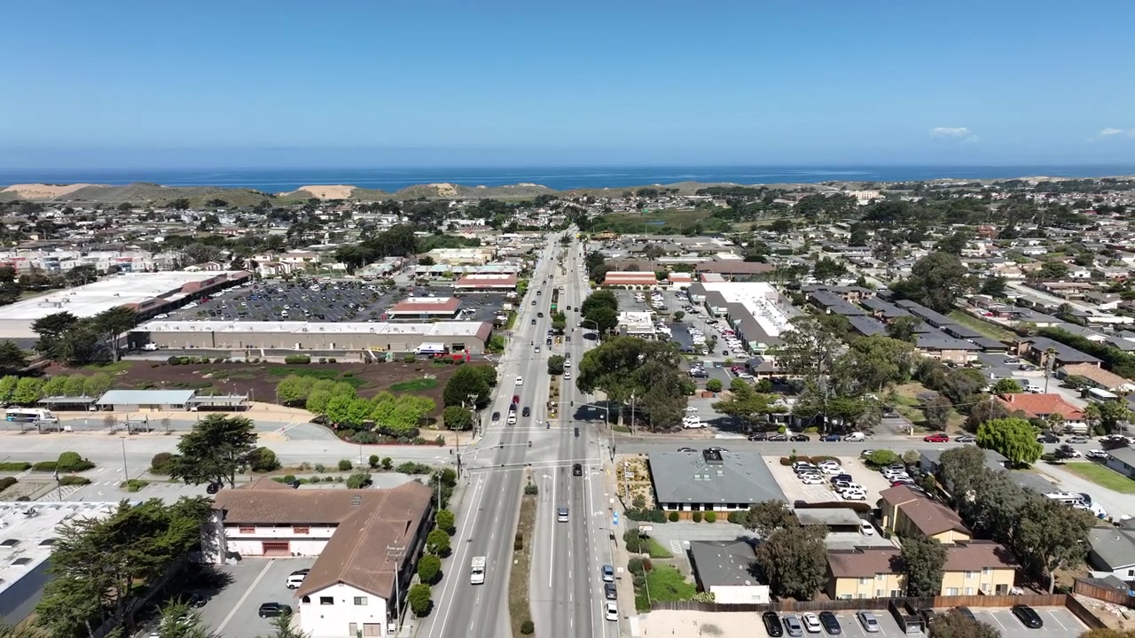 Riprese aeree cinematografiche con drone che volano all'indietro sopra Marina, California, mostrando vivaci quartieri commerciali, strade cittadine, centri commerciali, quartieri residenziali e grandi dune di sabbia costiere