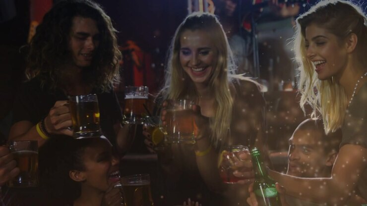 Amici al tavolo di un bar, suonano la chitarra, brindano facendo tintinnare bottiglie verdi e tazze, con effetto bokeh che attraversa l'inquadratura