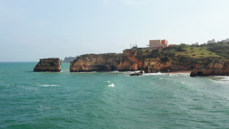 Aerial-drone-view-of-waves-crashing-against-colorful-Lagos-cliff-coastline,-drone-flying-foward-above-rocky-coast-reveal-amazing-sea-landscape,-day